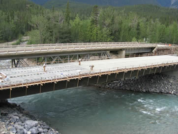 A bridge is above the river. On the surface of the bridge, three workers are working.